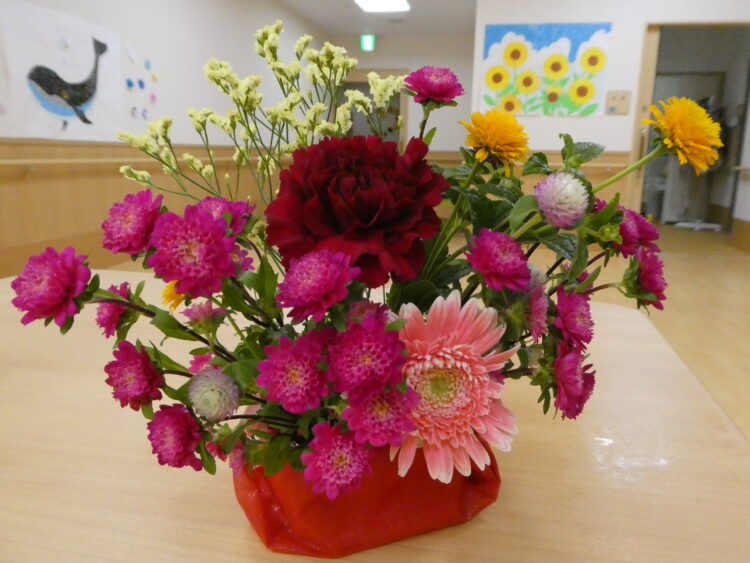 介護施設の共用部に飾られた色鮮やかな生け花。壁面装飾が見える。